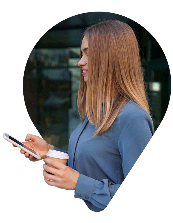 Side view of woman wearing a blue shirt, holding a mobile phone and cup of coffee. 